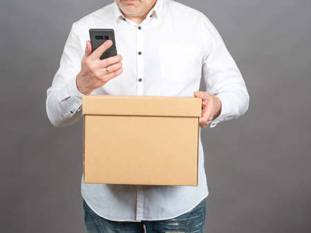 Sending parcel. Delivery mobile app. Call a courier online. Using courier service. Man with a cardboard box and a smartphone. Unrecognizable man with mobile phone and parcel.の写真素材