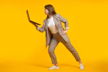 Modern businesswoman. businesswoman uses laptop. businesswoman in stylish clothes. She is posing on yellow background. Woman with open laptop in her hand. Girl in plaid suit. Stylish woman laptopの写真素材