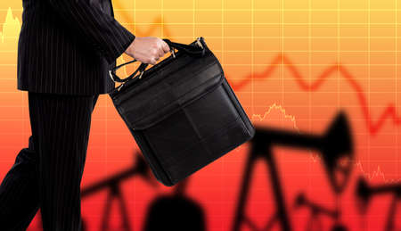 Trader on oil products exchange. Businessman with a black bag next to an oil pump. Concept - sale of petroleum products. Falling oil prices. Charts symbolize the fall in petrolium prices.の写真素材