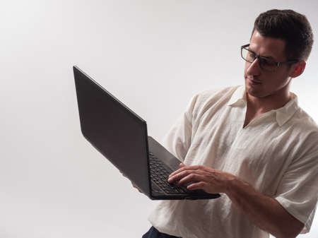 Computer master with a laptop in his hands. Portrait of computer master on light background. He is trying to set up computer. Concept - computer master configures software. System administrator.の写真素材