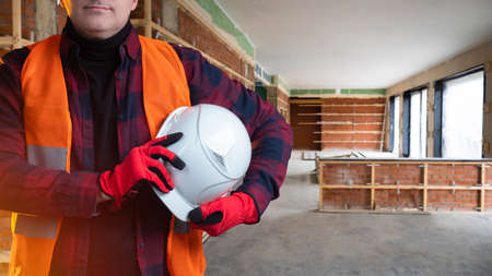 Architecture and construction. Repair of offices and apartments. An unrecognizable man holds a construction helmet in his hands. Person on a construction site. A man in a building under construction.の写真素材