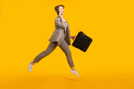 Happy manager woman. Successful woman manager on a yellow background. Girl with a business bag. Business briefcase in hand of happy woman. Happy girl with phone. She's talking on phone.の写真素材