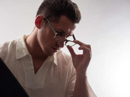 Man teacher adjusts his glasses. Portrait of a guy working as a lector. Guy on a white background. Man teacher is thinking about something. Pensive Man teacher. He teaches at school or collegeの写真素材