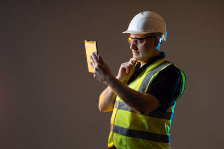 Builder tablet. Builder with a tablet computer. Portrait of adult worker in a construction uniform. Builder tablet is in his hands. Man working in a construction company. Architect Firm Employeeの写真素材