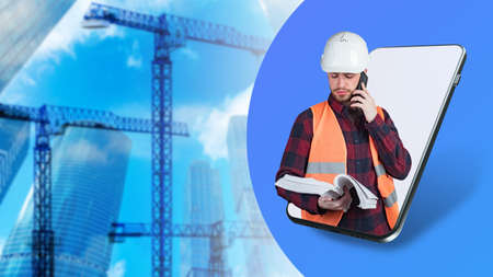 Construction engineer. Male builder at phone screen. Portrait of a guy in uniform of a builder. young engineer speaks on phone. Tower cranes next to a man. Architect engineer career concept.の写真素材