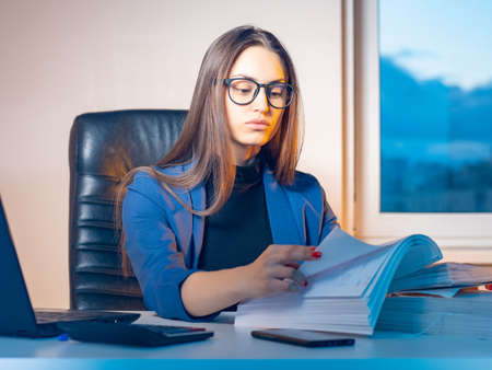 Woman lawyer. Businesswoman works in office. Woman is leafing through large folder of documents. Concept - career as lawyer. Woman works in legal office. Girl in blue at computer table.の写真素材