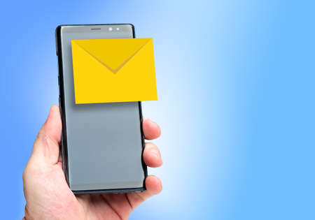 E-mail concept. Emails in a smartphone. The envelope icon on the smartphone screen. A person is holding a phone with an email program in his hand. Space for text on a blue background. 3d imageの写真素材
