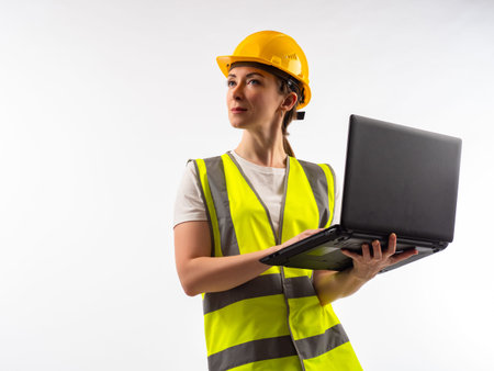 Woman in reflective vest and hard hat looks up. Girl engineer or builder. Engineer with laptop on a...