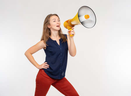 Large loudspeaker in woman's hand. Girl smiles and shouts into megaphone. She is trying to shout to someone. Loudspeaker symbolizes advertising. Girl advertiser on light background. Woman marketerの写真素材