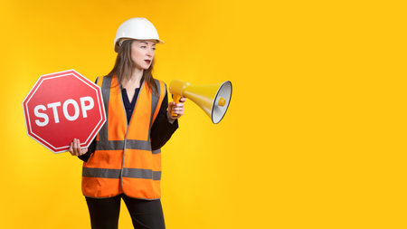 Woman with a loudspeaker and a STOP sign. Forbidding sign. Prohibition, termination, ban of activity. Introduction of restrictions. Woman in reflective vest informs about restrictions and prohibitionsの写真素材