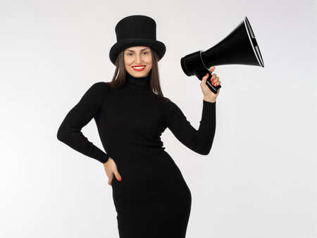 Slender girl with a loudspeaker. A woman in black clothes and a black top hat. The fatal beauty looks into the camera. A joyful girl shows off her figure. A girl in a tight black dress.の写真素材