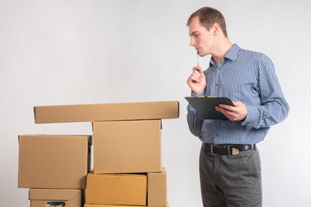manager with clipboard looks at boxes. Guy looks at cardboard boxes. Portrait of businessman on...