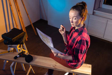 furniture making designer concept. Woman with architectural plan. Girl furniture maker in casual uniform. Carpenter woman. Planks beside woman carpenter. Girl furniture maker in carpentry workshopの写真素材
