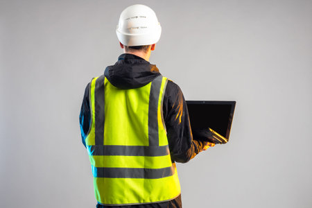 Worker with laptop. Man in protective uniform. Worker in hard hat holds open laptop. Portrait of...