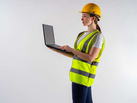 Woman inspector with a laptop in her hands. Girl inspector on a white background. She works as a reviewer somewhere. inspector with a computer in hand. Portrait of a girl in a yellow vest.の写真素材