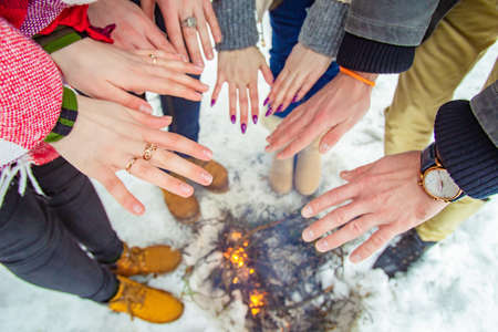 Hands warm over komtre. Concept - outdoor recreation. A group of friends warms his hands over the fire. Winter holidays in the forest. Hands of people over a smoldering fire. Cold. Snow.の写真素材