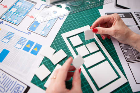 UX design. Application prototype. Phone application designer. The girl thinks what the mobile application will be. Designer desktop. Presentation of a phone app made of paper. Making appの写真素材