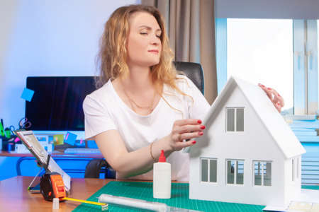 Architect glues the layout of the house. Work on an order at an architectural agency.Development of a building layout for presentation. Assembling a miniature copy of the house.Girl architect at workの写真素材
