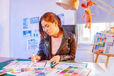 UX design. Girl draws a sketch of the future application.Mobile Application Development Company. Prototype mobile application.Woman designer. Development of programs for the smartphone.App for gadgetsの写真素材