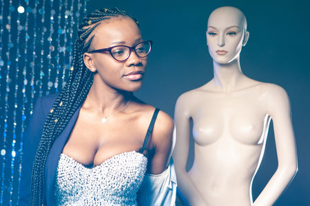 Girl in a clothing store.Concept-fashion designer. Model with a manikin in the background. Black woman in a fashion boutique. Girl trying on clothes. Dressing room. African American chooses an image.の写真素材