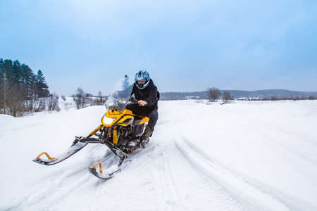 Man rides a snowmobile. Concept - speed. Concept - the absence of obstacles. Winter Snowmobile Race. Extreme sport. Snowmobile rides at high speed. Snowmobiler. Driving on snow-covered terrainの写真素材