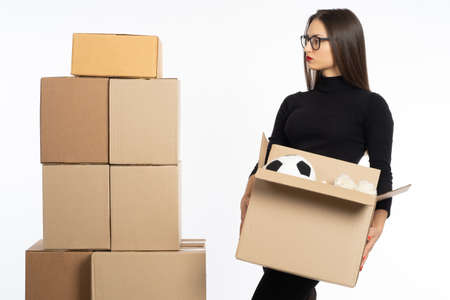 Girl with open box. Woman changes housing concept. Cardboard boxes next to girl is holding box of toys. Unpacking wild things when changing housing. Girl in black on light background. Girl home moverの写真素材