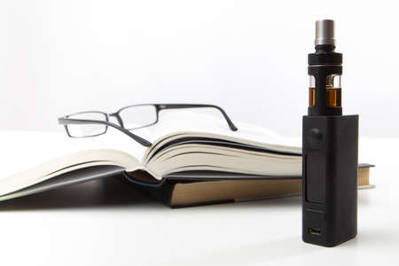 Vape. Vape machine next to the book. Concept - vaper is reading a book. The concept is to relax after work. Reading Glasses. Vaping. Rest for the vaper. A device for vape. E-Sigs. Gift for the vaperの写真素材