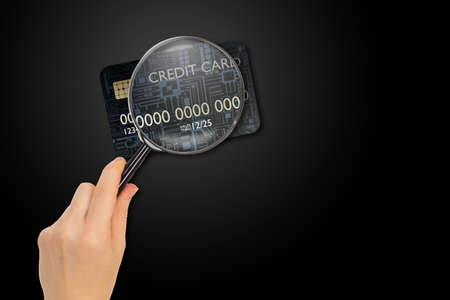 Credit card under magnifying glass. Concept - analysis of conditions of bank card. Research on loan products. Verification of banking transactions. Hand with magnifying glass on dark backgroundの写真素材