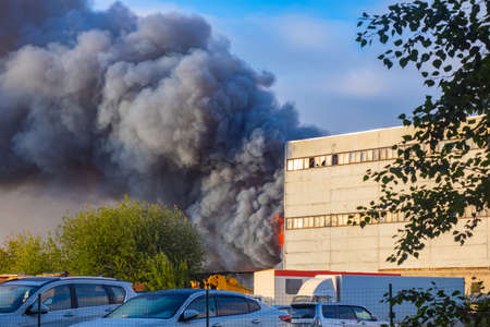 Smoke over enterprise building. Smoke from fire. Black clouds of smoke over enterprise. Black clubs fume next to concrete structure. Concept fire in chemical plant. Black fume from burning chemicalsの写真素材