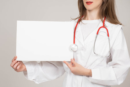Woman doctor shows banner. Medic shows sheet of paper. Blank banner in hands of nurse. Concept - doctor recommends something. Place for inscription in hands of doctor. Private clinic employeeの写真素材