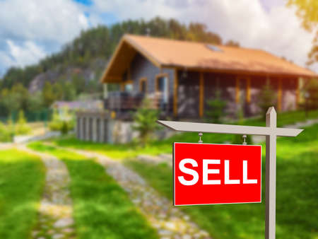 Sell sign near house. Red sell sign near cottage. Sale of country cottage. Country house with inscription sell. Sale of suburban real estate. House at foot of mountain. Selective focusing.の写真素材