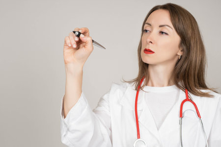 Doctor with marker. She writes something on virtual screen. doctor holds out marker to screen. Concept - she writes something on virtual screen. Serious doctor. Clinic worker woman.の写真素材