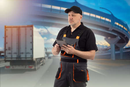 Automotive logistics. Logistics man with tablet. Concept - work as dispatcher-logistician. Employee of logistics company. Blurred truck under bridge in background. Dispatcher-Logistician career.の写真素材