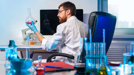 Forensic Laboratory. Lab technician examines a sample. Man with a flask in his hands. Scientist looks at reagents. Sanitary and Hygienic Laboratory. Biological fluids. Chemist at the computer tableの写真素材
