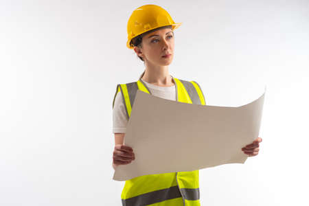 Woman architect. Architect in construction uniform. Sheet of paper in hands of builder. Portrait architect on white background. Young girl builder. Employee of architectural bureau. Engineer careerの写真素材
