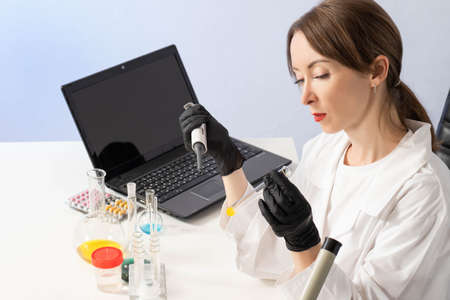 Laboratory technic Scientist at workplace. Laboratory technican with test tube in hand. She is analyzing something. Laptop next to lab technic Medical lab employee girl. Scientist career.の写真素材
