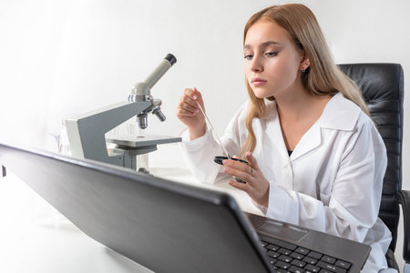 Medical research. Woman scientist in white coat. Doctor with microscope. laboratory assistant looks at laptop. doctor is doing research. Blonde woman doctor. Career in medical laboratory.の写真素材