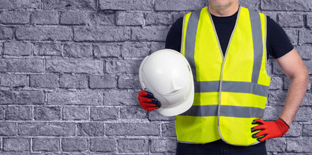 Working foreman next to wall. Builder with white hard hat. Human in builder uniform. Foreman without...
