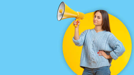 Megaphone in woman's hand. Girl with megaphone on yellow-blue. Loudspeaker as metaphor for agitation and propaganda. Teenage girl has big loudspeaker. Copy space for your proposal. Place for ads.の写真素材
