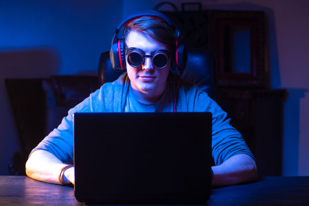 Guy in the headphones and sunglasses. Man in headphones plays games. Concept - video games on a laptop. Studen listens to music. Recreation. Concept - selling headphones. Gambling addiction.の写真素材