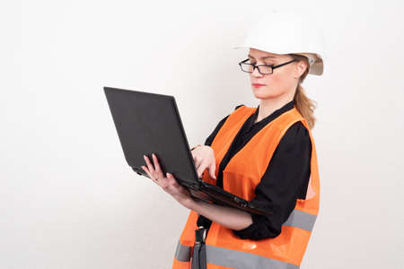 female engineer. Girl with a laptop in a reflective vest. Girl in a protective yolk and helmet. A woman works in a dangerous place. Girl standing working with a laptop. Engineer at the enterpriseの写真素材