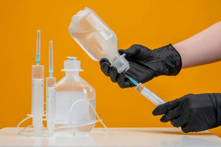 A man takes fluid from a dropper. A doctor draws a medicine into a syringe. disease treatment. Drugs against infectious diseases. Hands in gloves hold a dropper. Concept - treatment with medicationsの写真素材