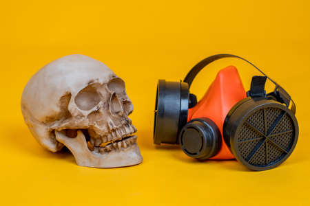Human skull next to a respirator. Skull and a respirator on an orange background. Concept - security measures during an epidemic. Fever is transmitted through the air. Caution in the study of virusesの写真素材