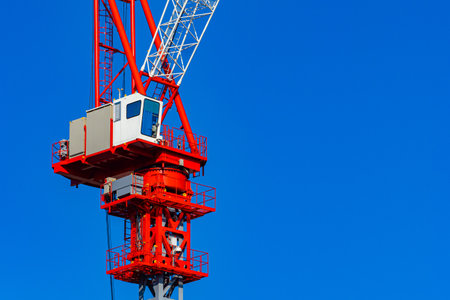 building. Red crane on the background of blue sky. Crane cabin close-up. Crane operator cabin on blue sky background. Jenny. Work on a construction site. Sale of construction equipment.の写真素材