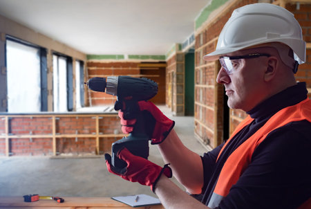 Builder screwdriver. Man repairman at construction site. Worker safety helmet. Repairman grandfather...