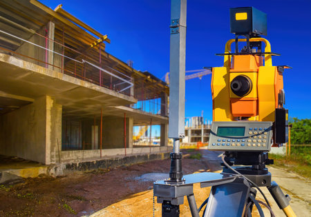 Equipment for surveyor. construction site. Geodetic device on tripod. Gadget for work of surveyor. House under construction under blue sky. Yellow geodetic device. Equipment for builder - surveyorの写真素材