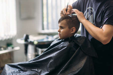 Little Boy Getting Haircut By Barber While Sitting In Chair At Barbershop.の写真素材
