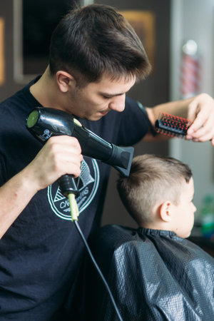Little Boy Getting Haircut By Barber While Sitting In Chair At Barbershop.の写真素材