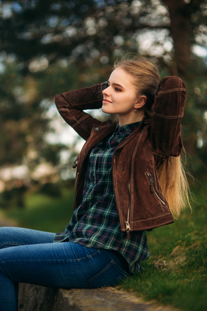 A beautiful girl is walking along the embankment. Blond hair and brown jacket. Spring.の写真素材