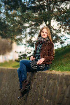 A beautiful girl is walking along the embankment. Blond hair and brown jacket. Spring.の写真素材